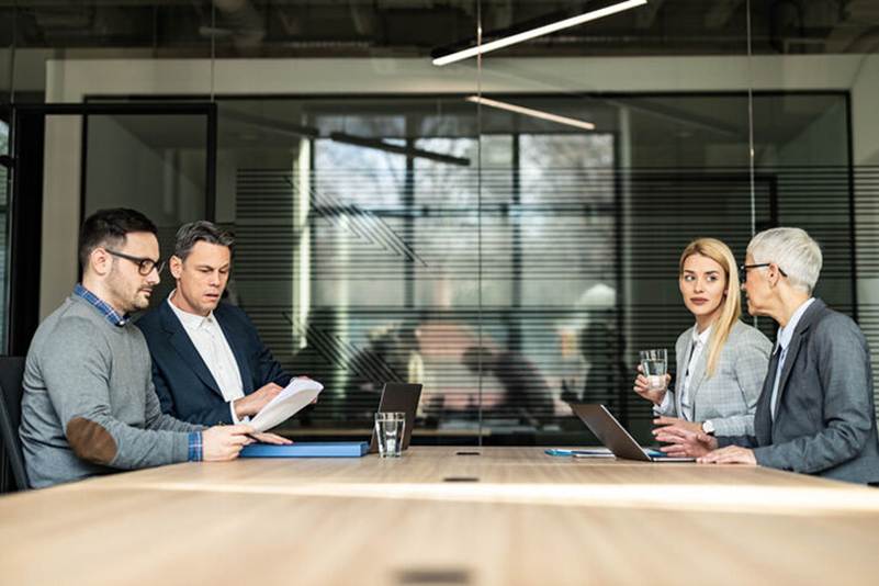 Four colleagues meet around a conference table, reviewing documents and laptops. This image could represent content creation or a team collaboration project on a website.